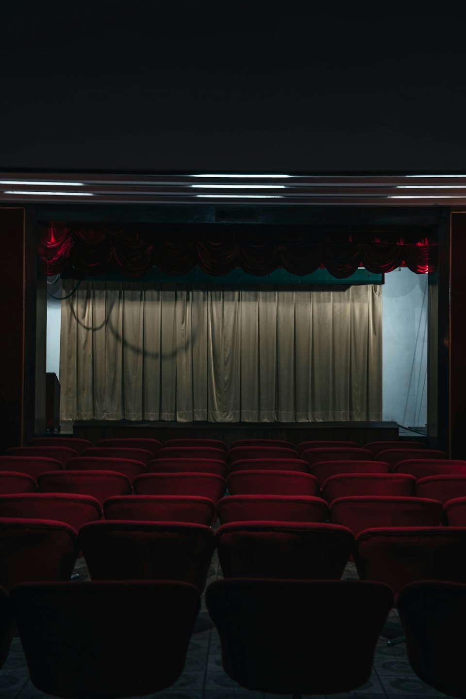 Leerer Theatersaal mit Sitzreihen, die auf eine Bühne ausgerichtet sind.