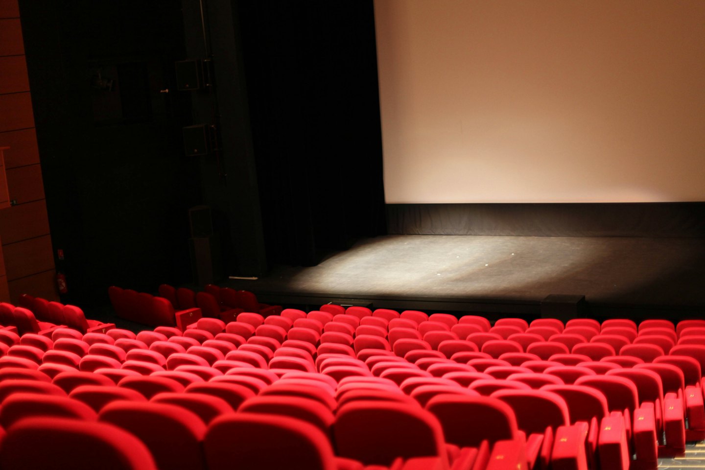 Leerer Hörsaal mit roten Sitzen, die auf eine beleuchtete Bühne gerichtet sind.